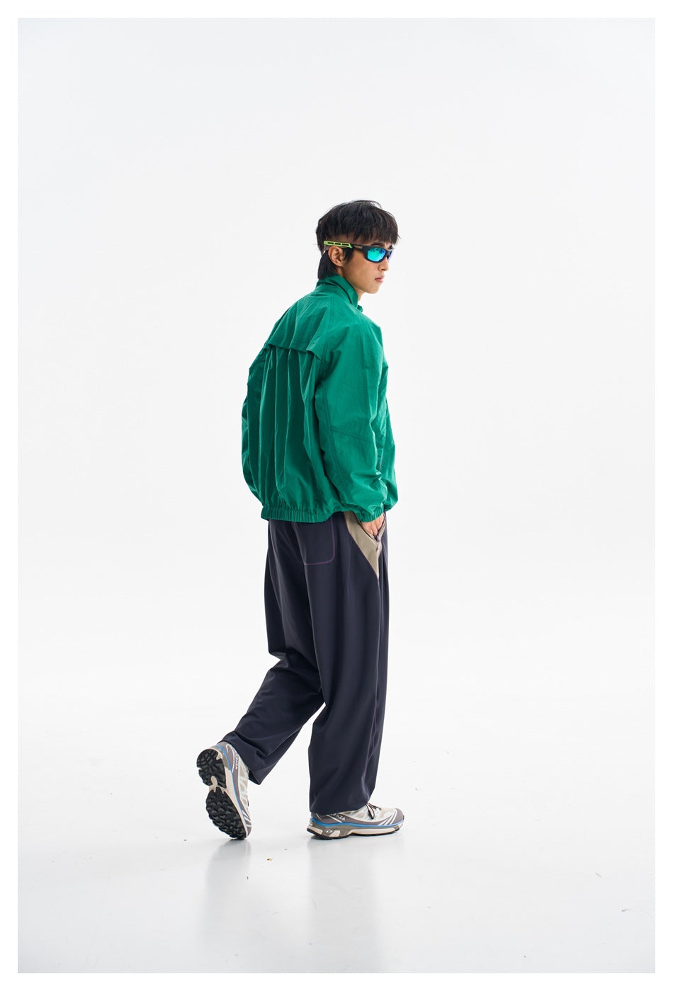 Side and rear view of a model wearing a teal-green zip jacket with dark wide-leg trousers.