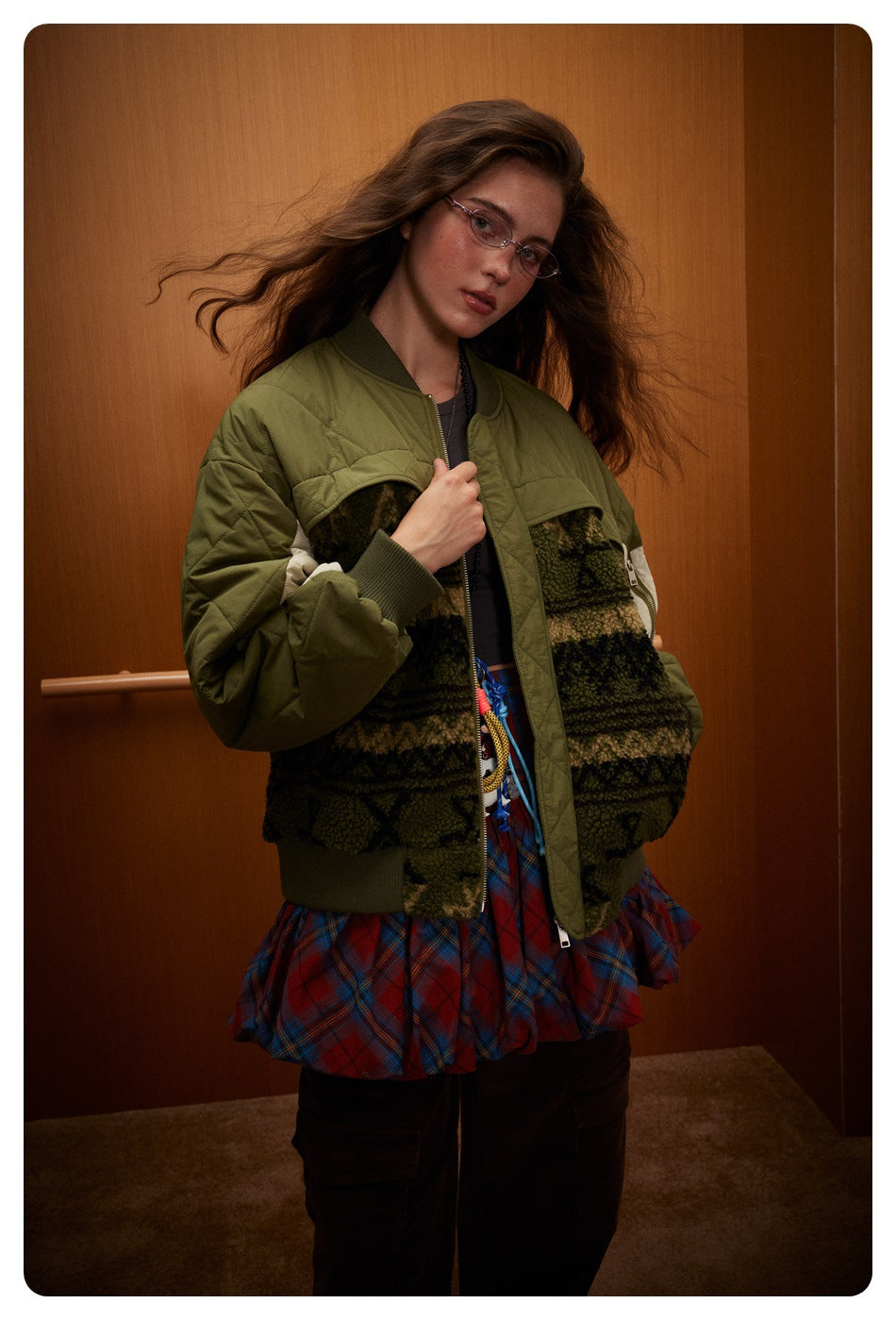 Model in a front three-quarter view of an olive quilted bomber jacket with cream panels and patterned fleece sections.