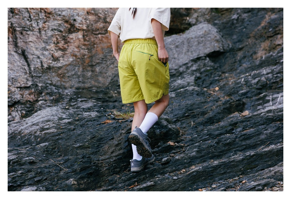 Rear view of a person wearing yellow-green shorts with a zip pocket while walking across rocks.
