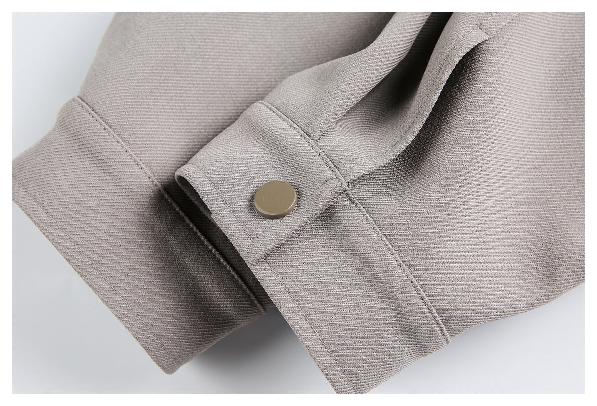 Close-up of a taupe garment cuff with a round matching snap button and visible stitching.