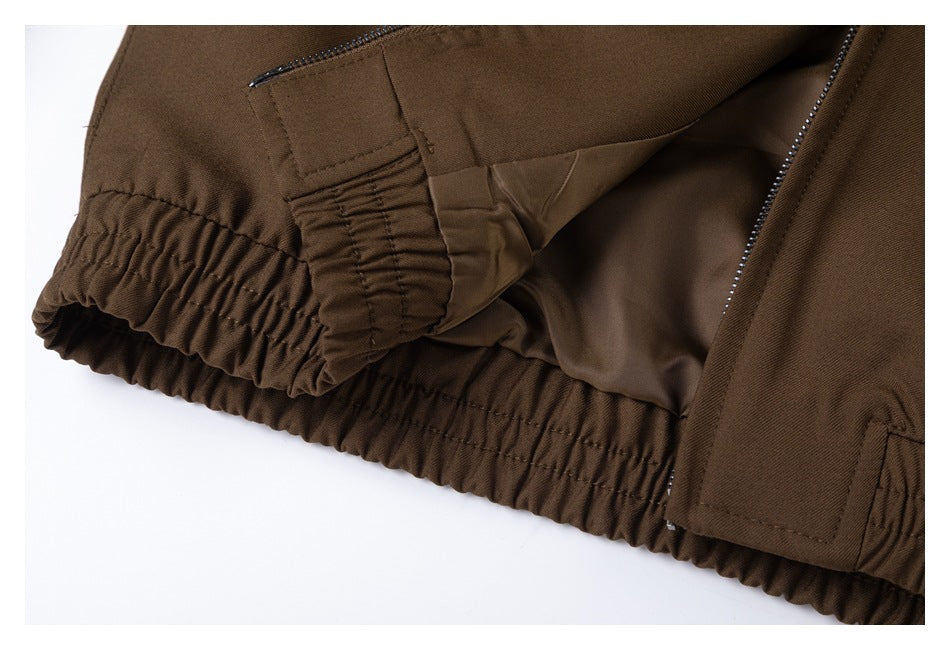 Close-up of a brown jacket's elasticated hem, zipper, and stitched adjustment tab.