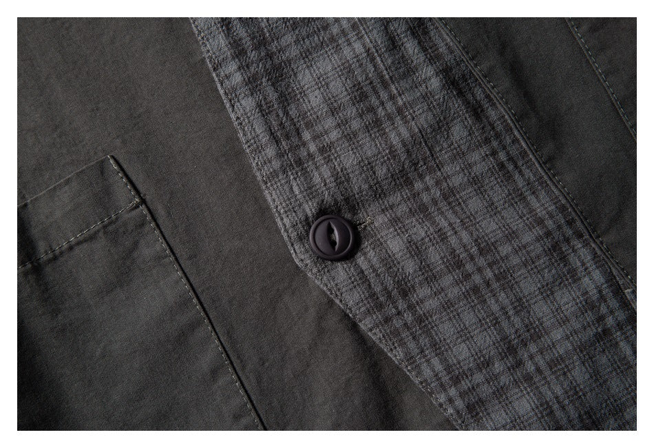 Close-up of a dark button on a gray plaid garment panel, with charcoal fabric and pocket edge.