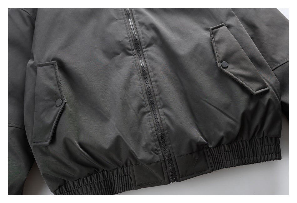 Close view of a charcoal jacket front with a center zipper, snap-flap pockets, and an elasticized hem.
