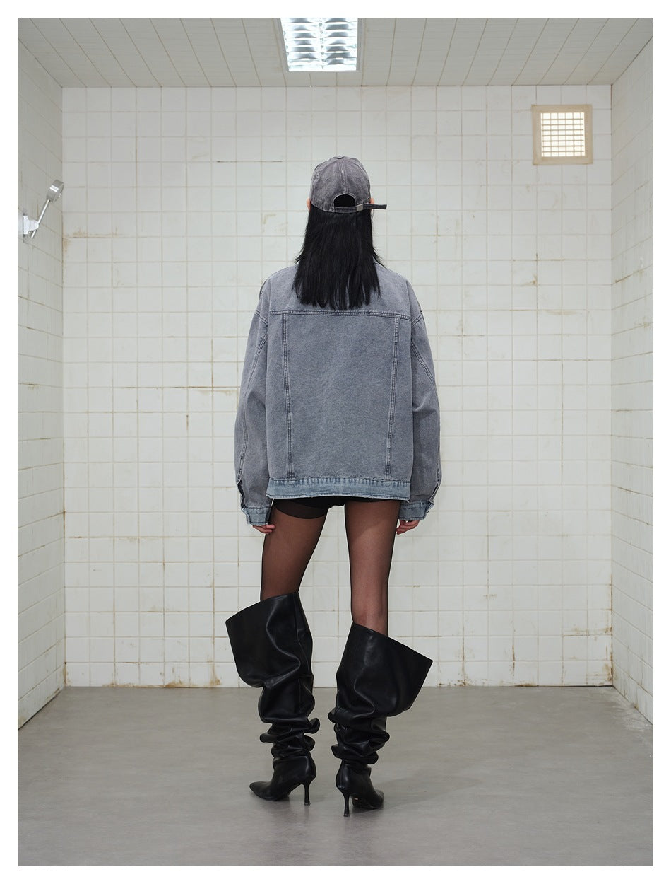 Back view of a model wearing an oversized gray denim jacket with a plain panel back and black boots.