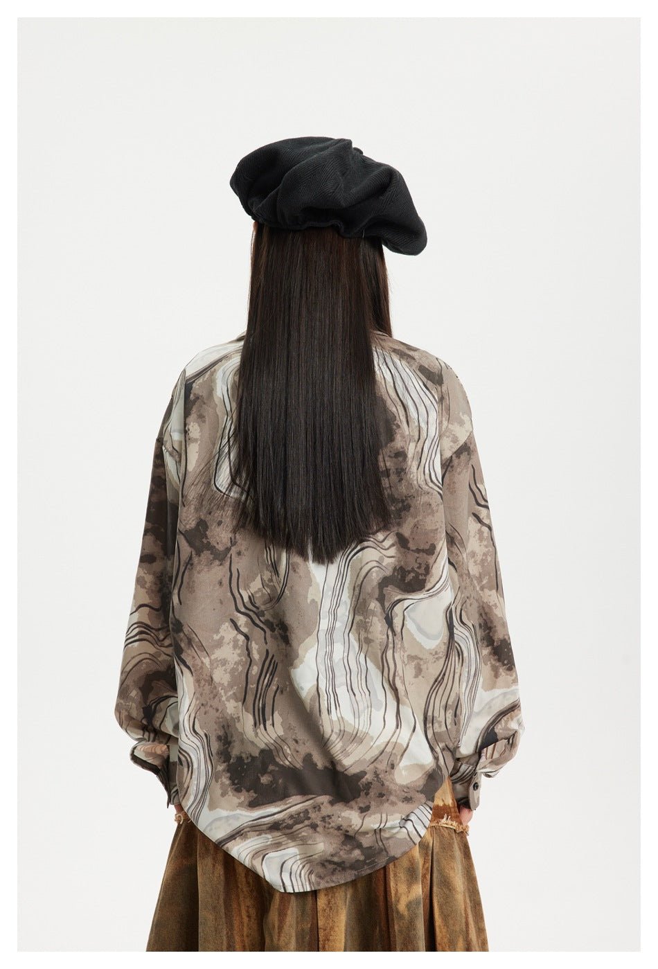 Rear view of a model wearing a taupe and cream abstract-print shirt with a rounded hem.