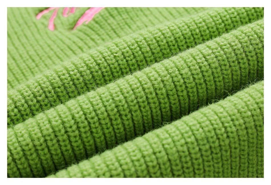 Macro view of folded bright green ribbed knit fabric, with part of pink embroidery visible in the background.
