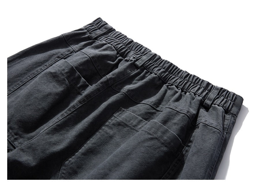 Close-up of charcoal trousers with a gathered elastic waistband, belt loops and patch pockets.
