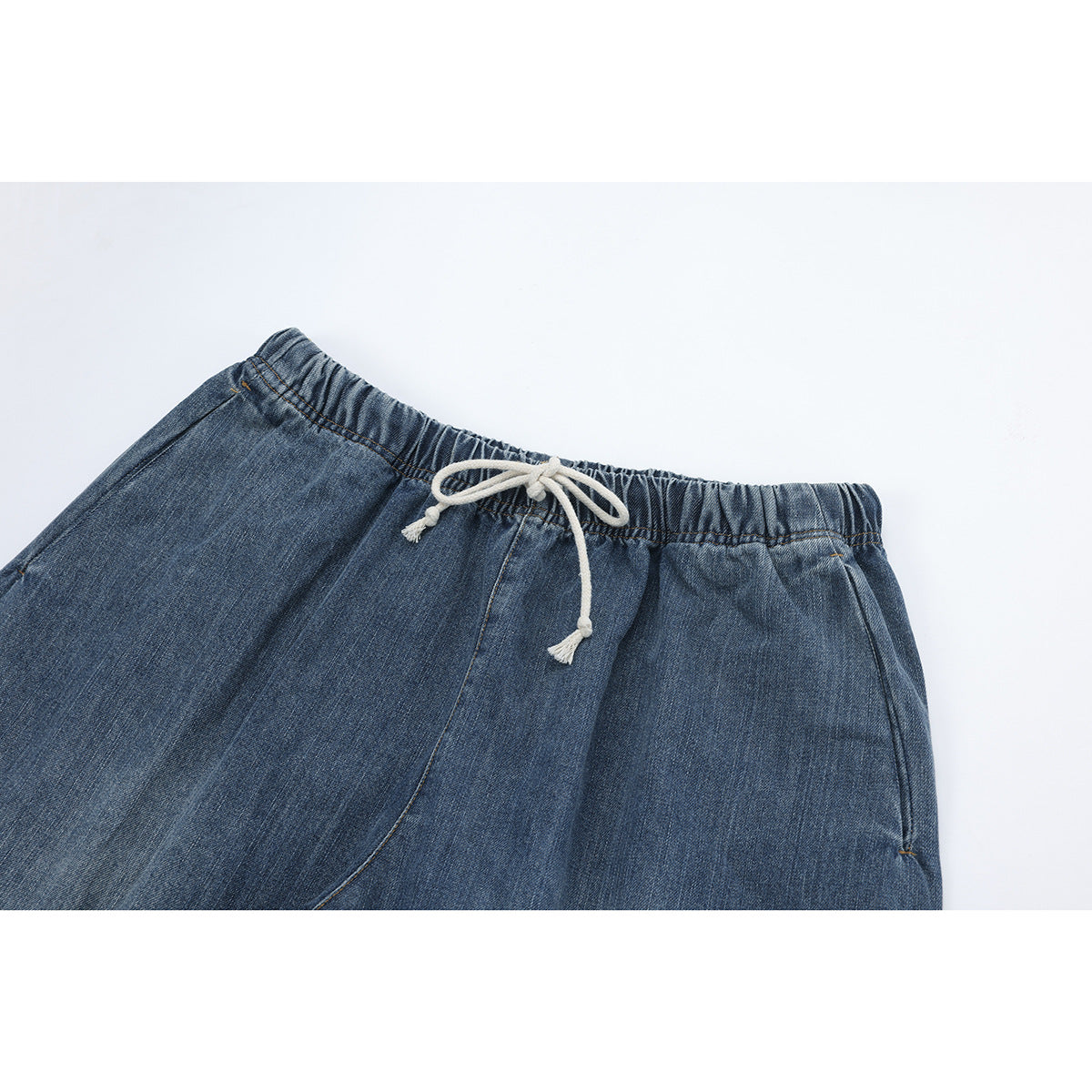 Close-up of blue denim pants with an elastic waistband and cream drawstring.