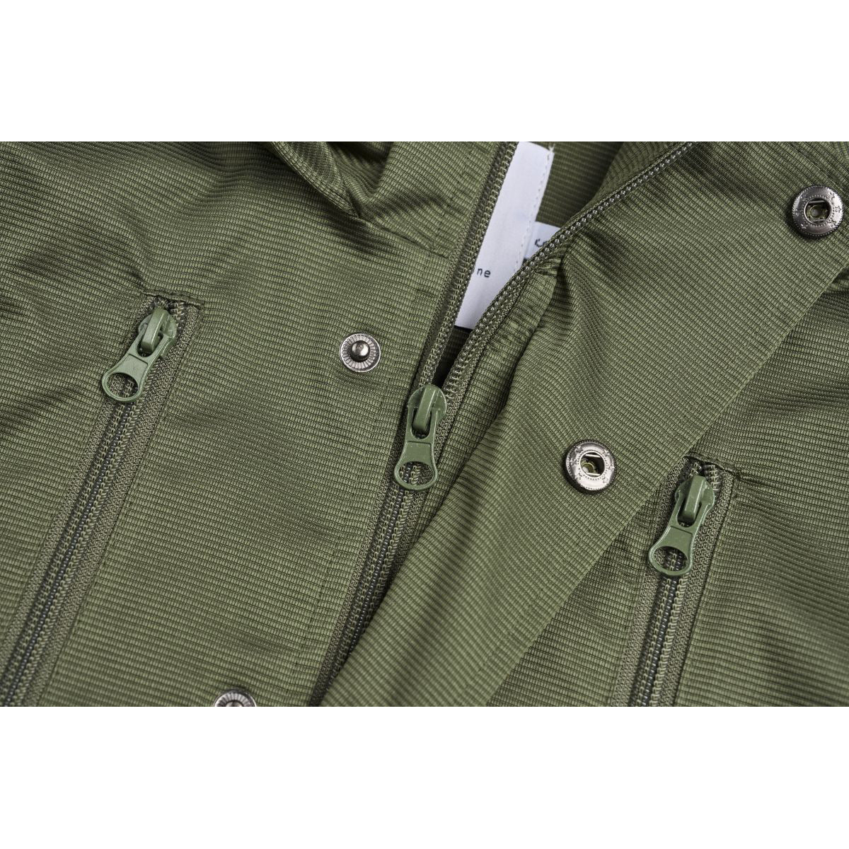 Close-up of an olive-green vest front with several zippers and metal snaps.