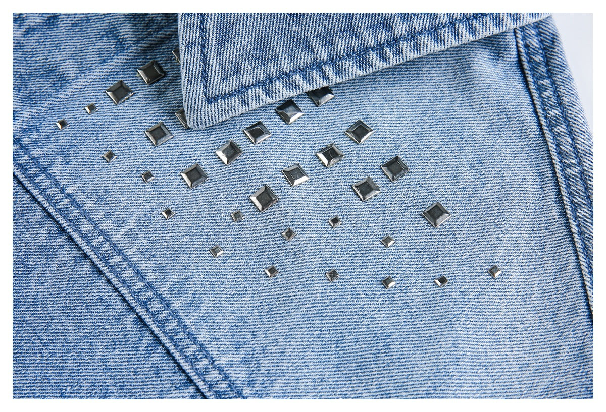 Close-up of square silver studs arranged across light blue denim beneath a jacket collar.