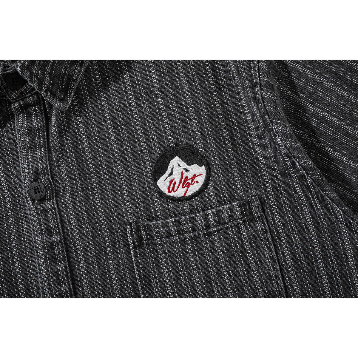 Close-up of a charcoal pinstriped shirt's chest pocket, buttons, and embroidered mountain patch.