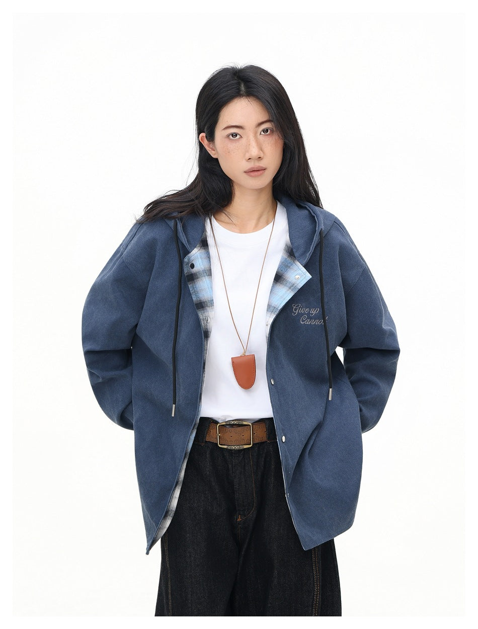 Model wearing an open solid blue hooded jacket with plaid lining, over a white shirt and dark jeans.