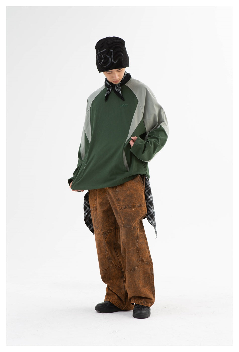 Model looking down while wearing the green color-block long-sleeve top with brown washed wide-leg pants and a black beanie