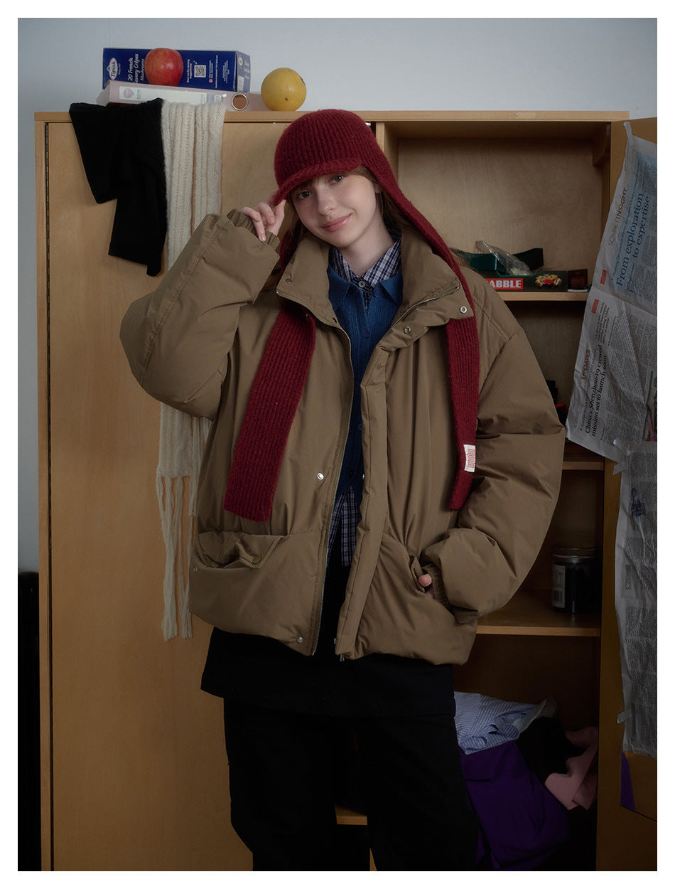 Front view of a model in a roomy taupe padded jacket with large pockets, styled with a burgundy knit hat and scarf.