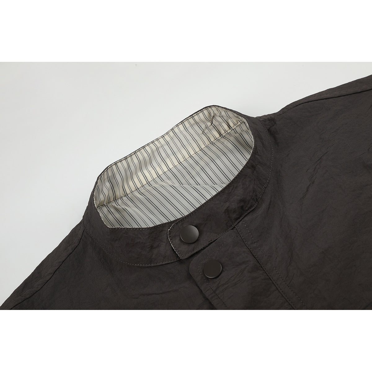 Close-up of a dark charcoal jacket's stand collar, striped inner lining, and snap-button placket.