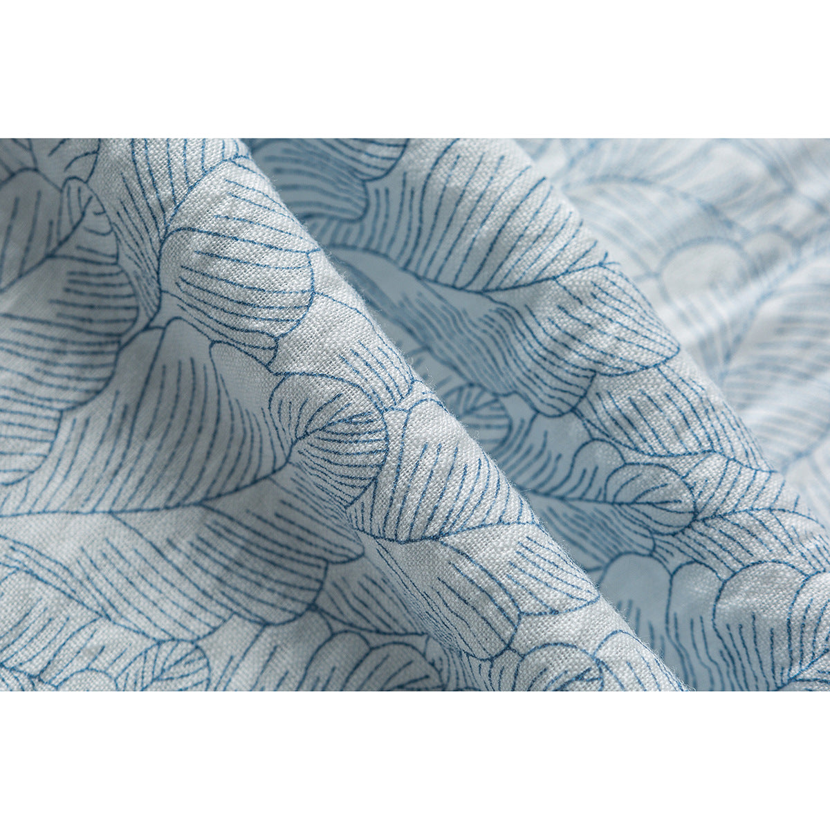 Macro view of the blue leaf print and visible weave on pale shirt fabric.