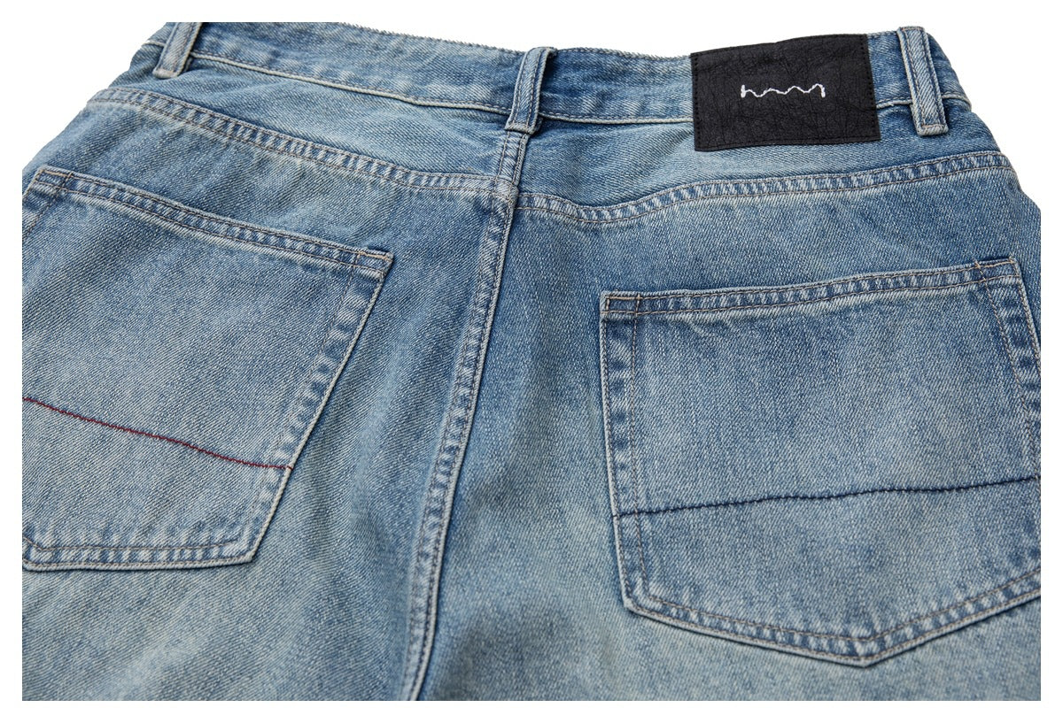 Cropped rear view of light blue washed jeans with two back pockets and a black waistband patch.
