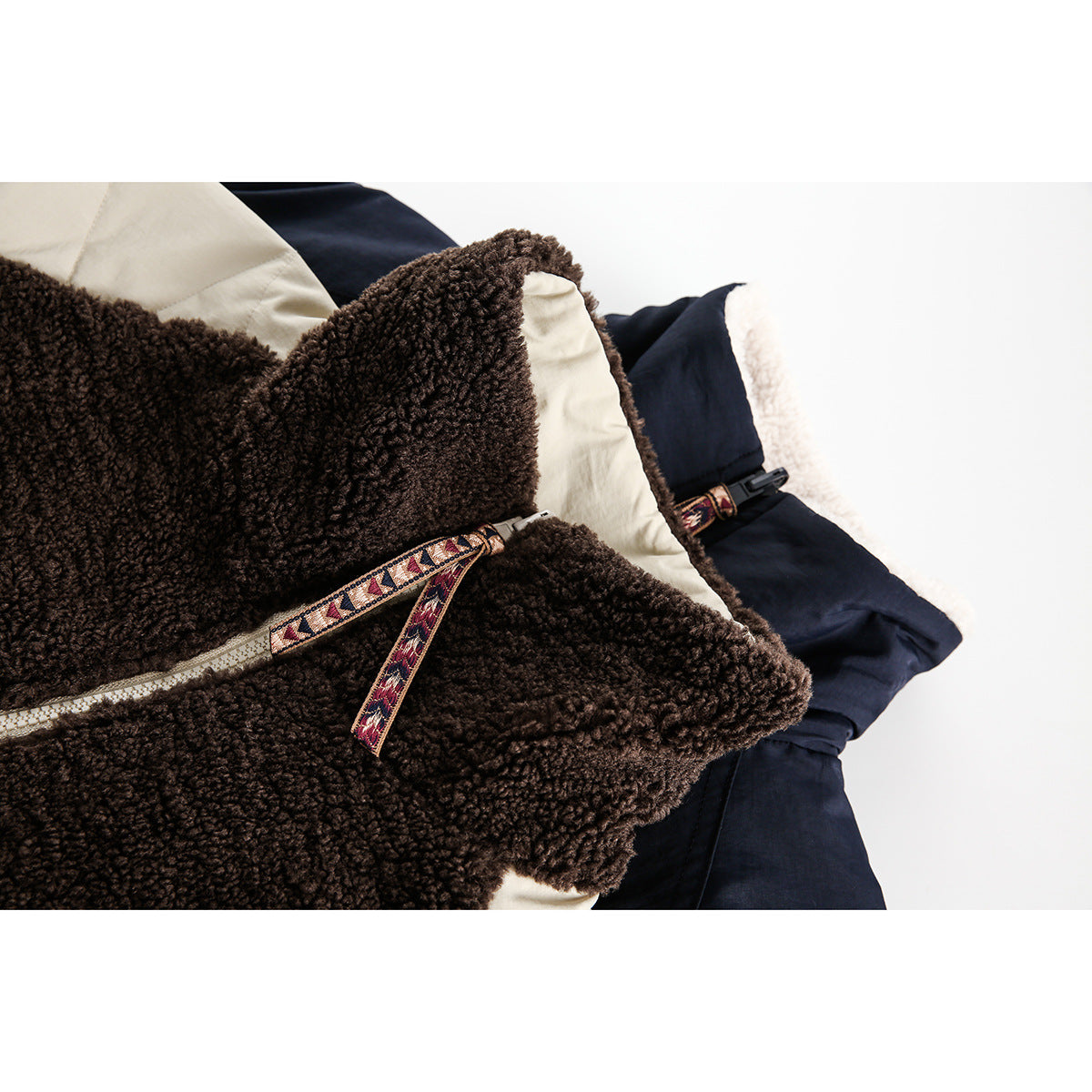 Close-up of folded dark brown sherpa and navy jackets with cream panels and patterned zipper pulls.