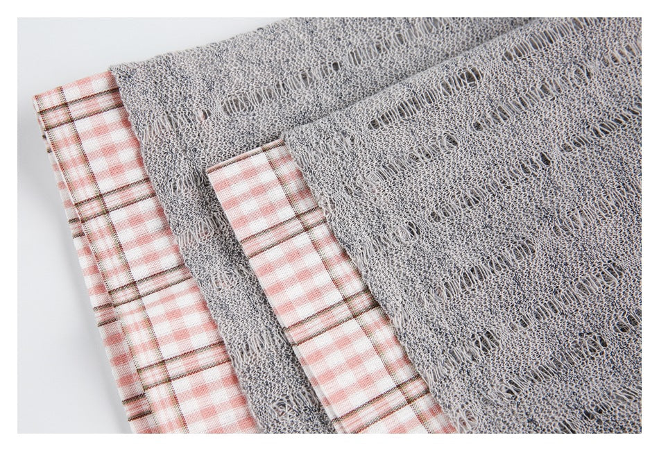 Close-up of the gray open-knit sweater and exposed pink plaid shirt fabric beneath it.