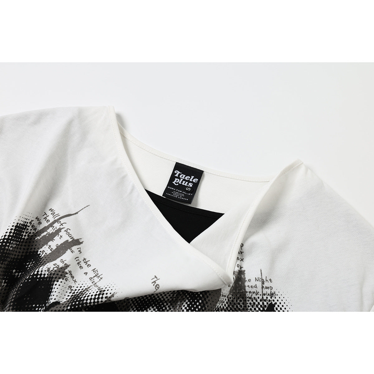 Close-up of a white wrap-neck shirt showing its black inner layer, sewn neck label, and part of a black graphic print.
