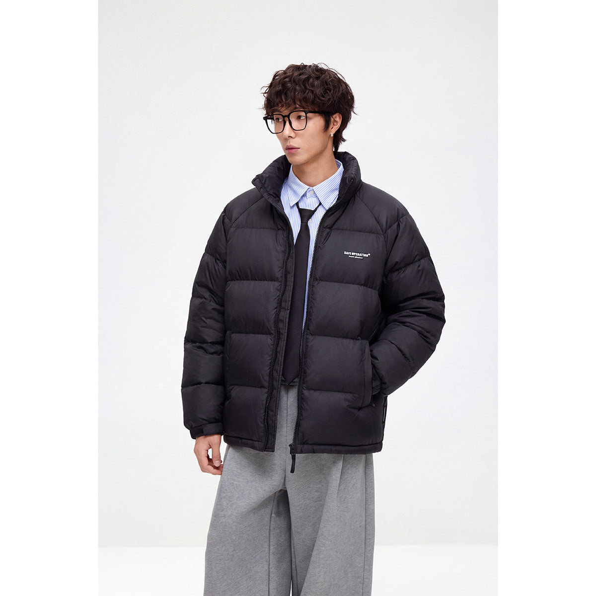 Model wearing a black quilted puffer jacket with a high collar, styled over a striped shirt and tie.