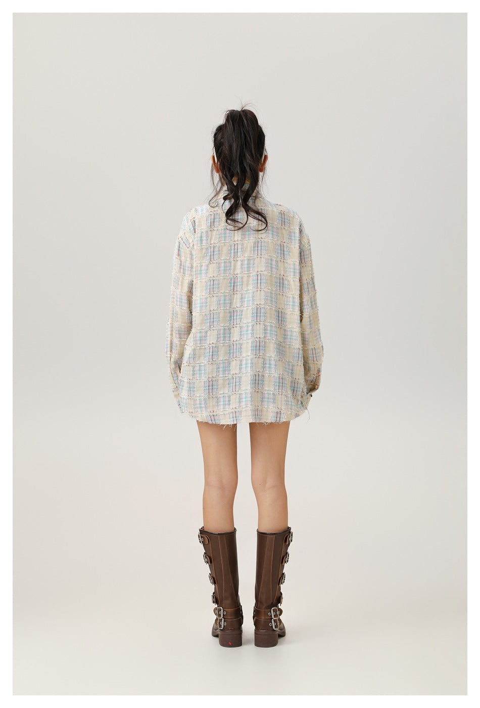 Back view of a model wearing a cream pastel-plaid oversized shirt with a curved hem.