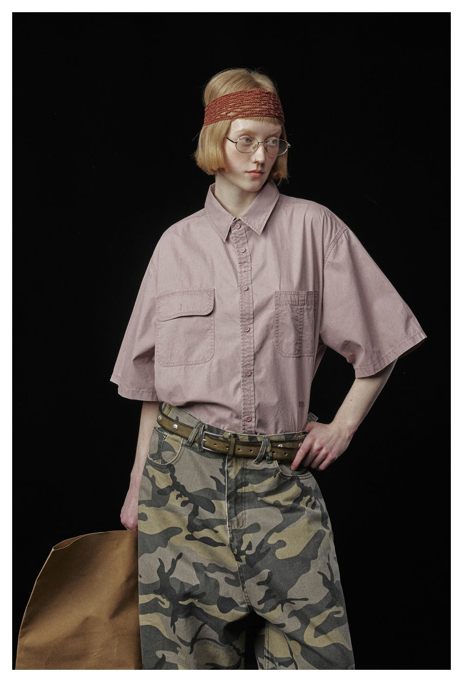 Model wearing a dusty pink button-up shirt with two chest pockets and loose camouflage pants.