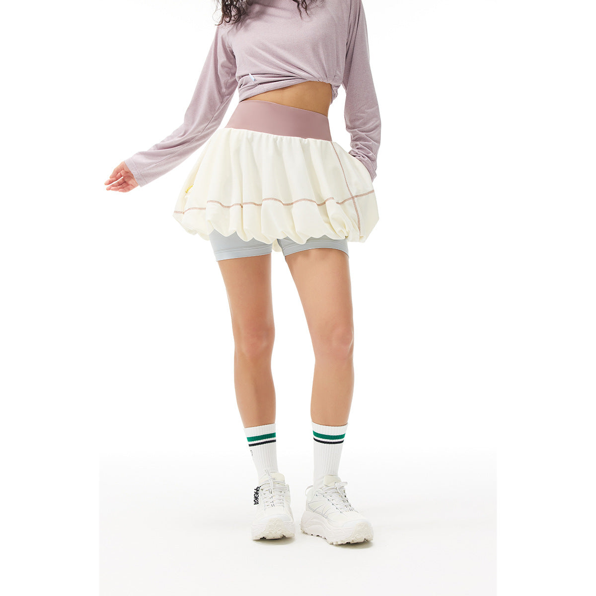 Rear view of a model wearing a white bubble tennis skirt with a pink waistband and light gray built-in shorts.