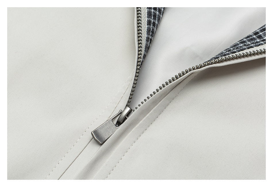 Close-up of a metal zipper on light beige fabric, with black-and-white plaid visible at the opening.