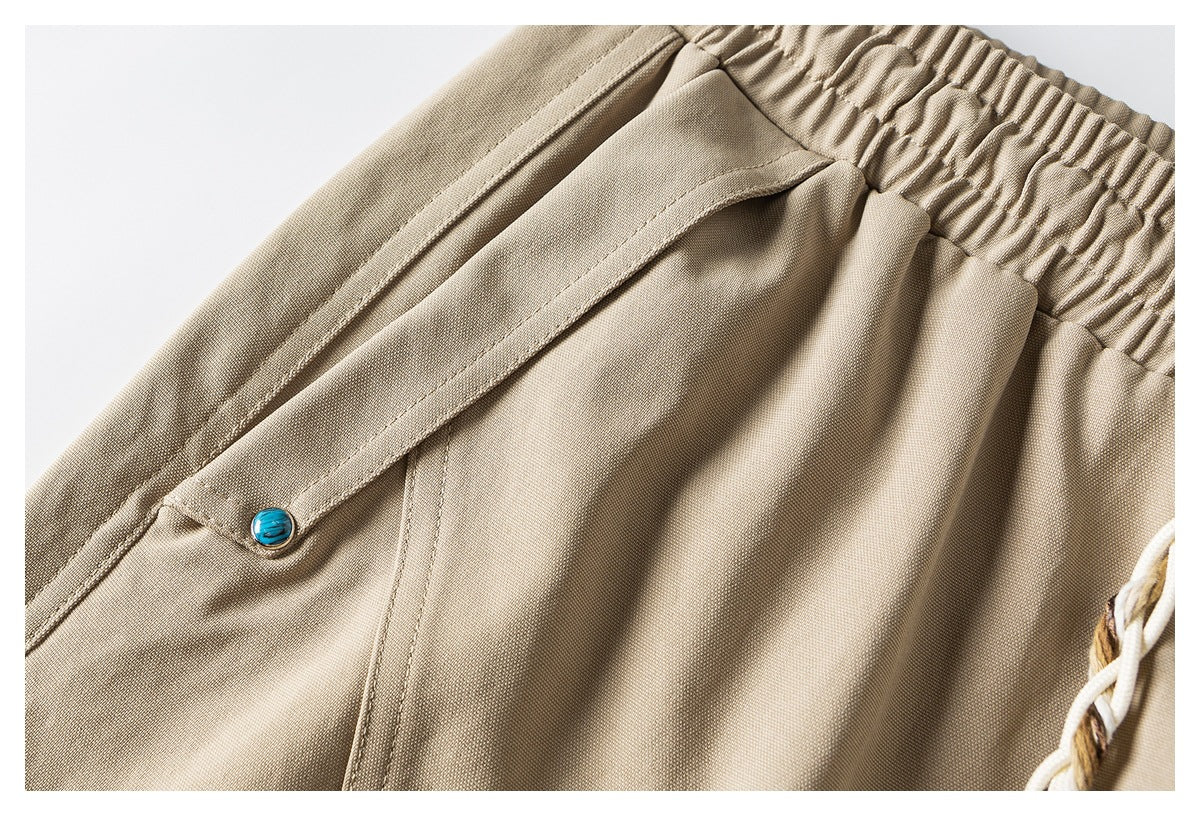 Khaki shorts close-up showing a flap pocket with a turquoise button and a gathered elastic waistband.