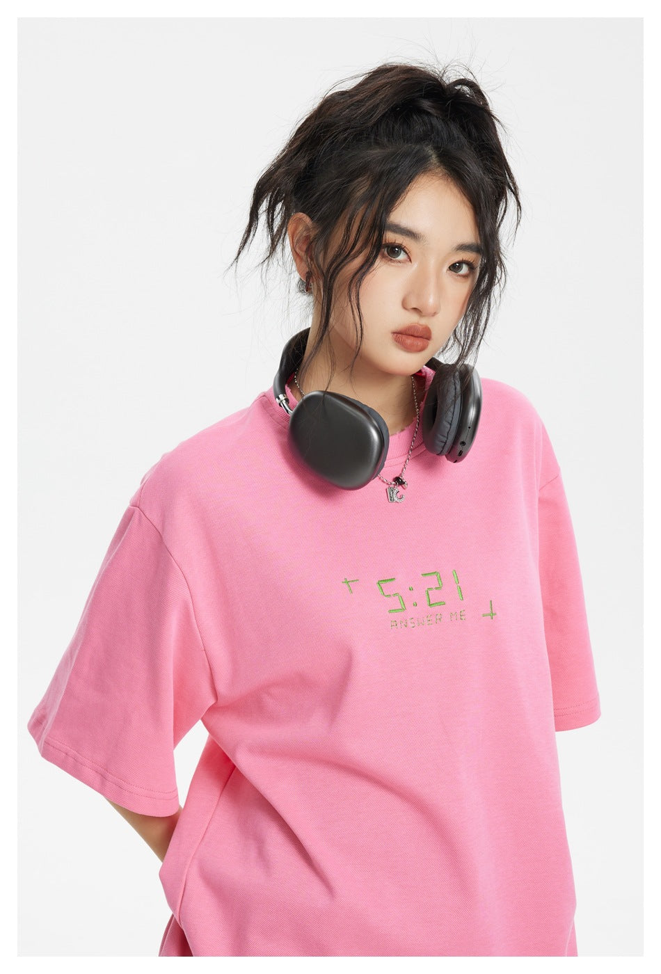 Close-up of a model wearing a bright pink T-shirt with small green chest lettering and wide sleeves.