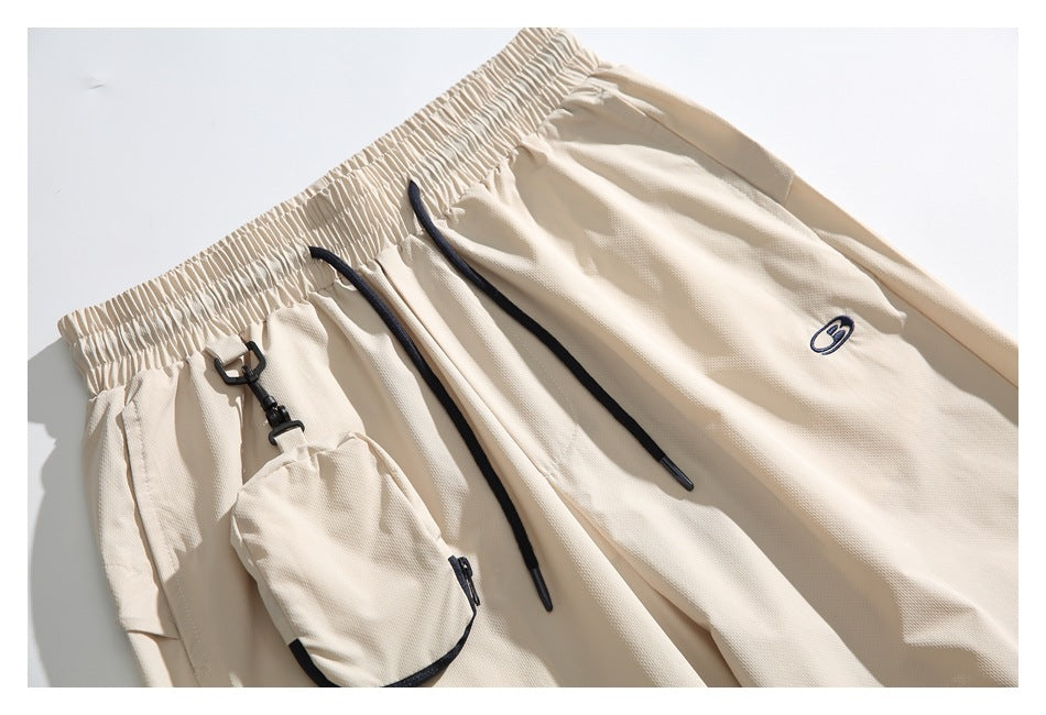 Close view of cream pants with black drawstrings, a clipped-on pouch, and a small embroidered emblem.