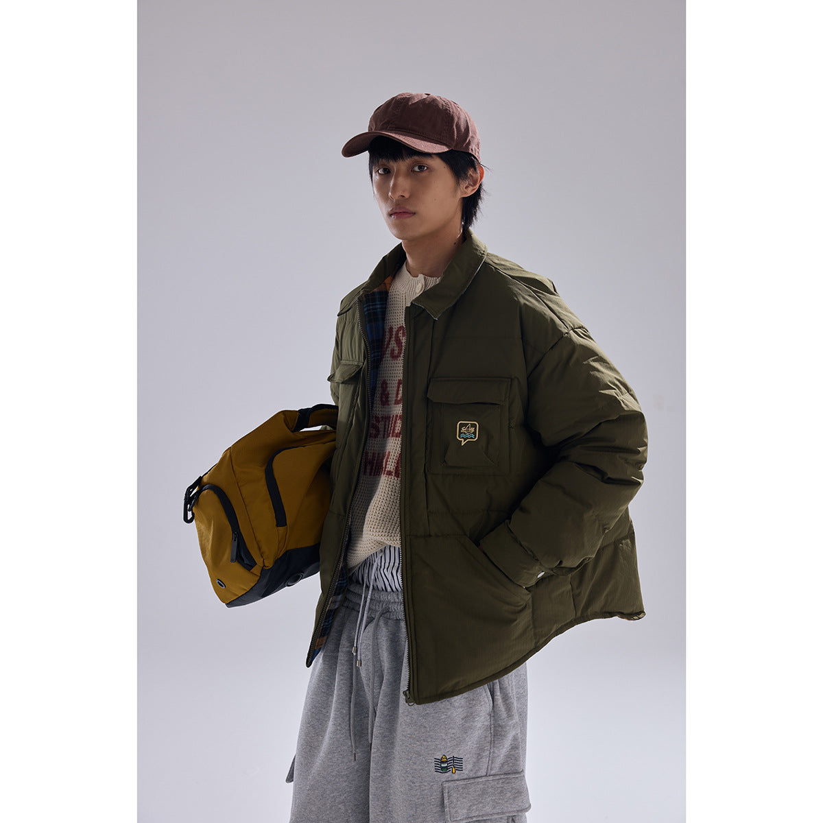 Model wearing an olive quilted jacket with flap chest pockets, a cream sweater, and gray cargo pants.