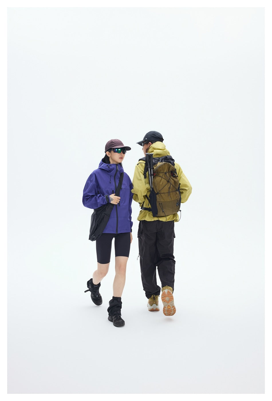 Two hikers walk away, showing a purple jacket and a yellow hooded jacket with a brown backpack.