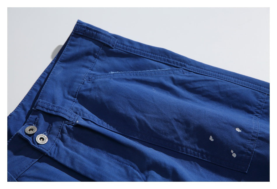 Close-up of royal-blue trousers with a flap pocket, two metal buttons, and small white paint-like marks.