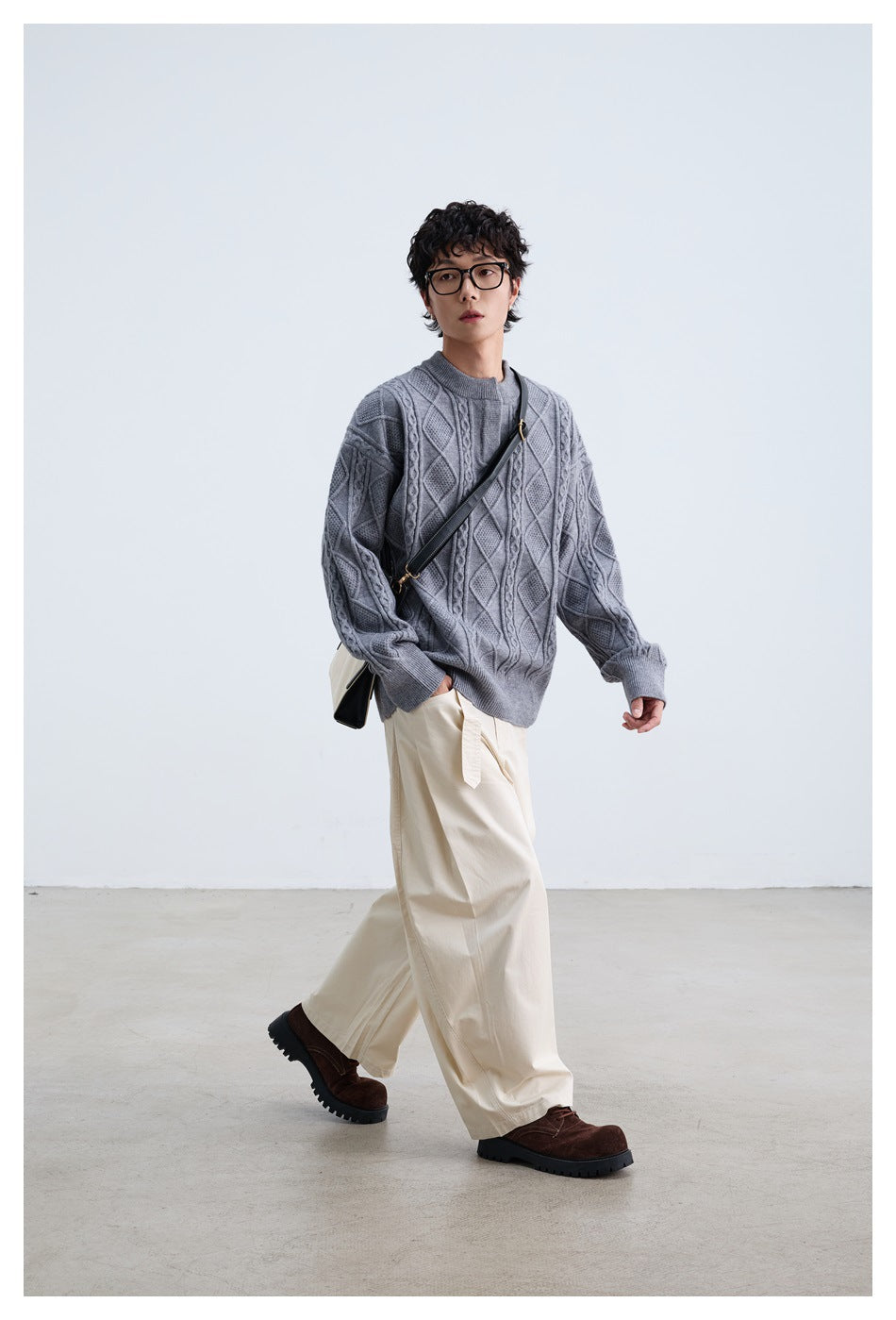 Model walking in a gray cable-knit sweater, cream wide-leg pants and brown shoes with a crossbody bag
