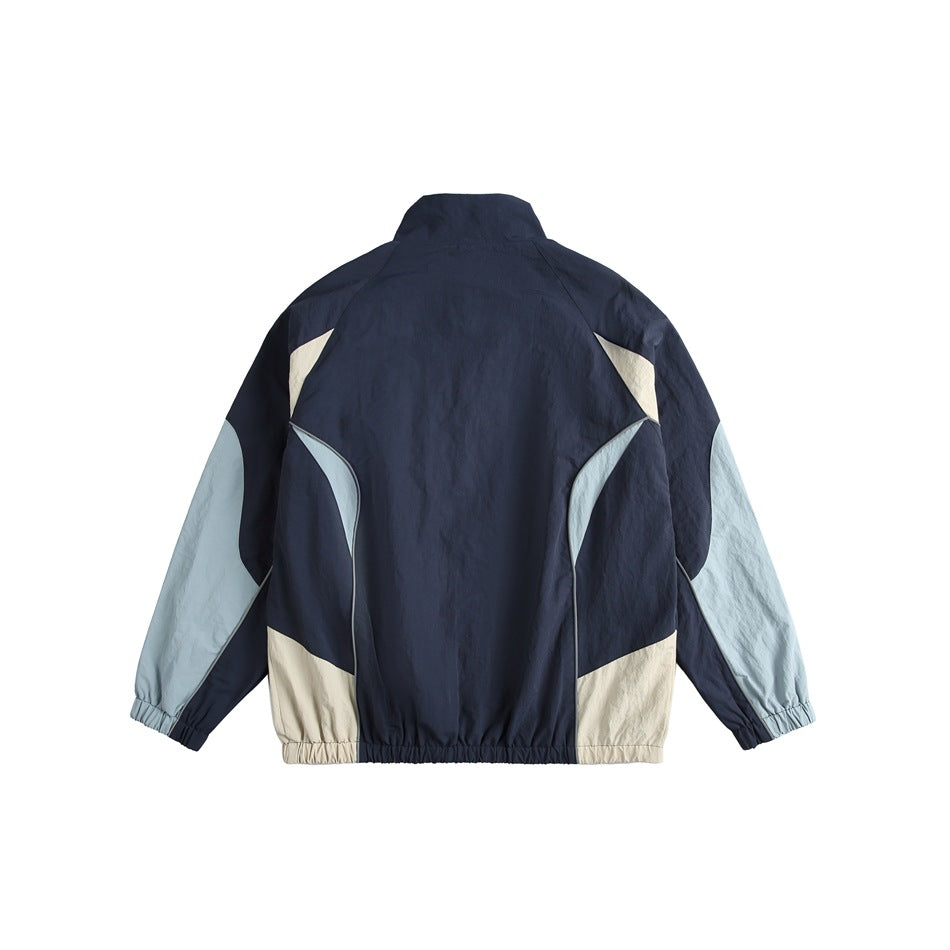 Back view of a color-block track jacket with a navy body, pale blue sleeves, and cream panels.