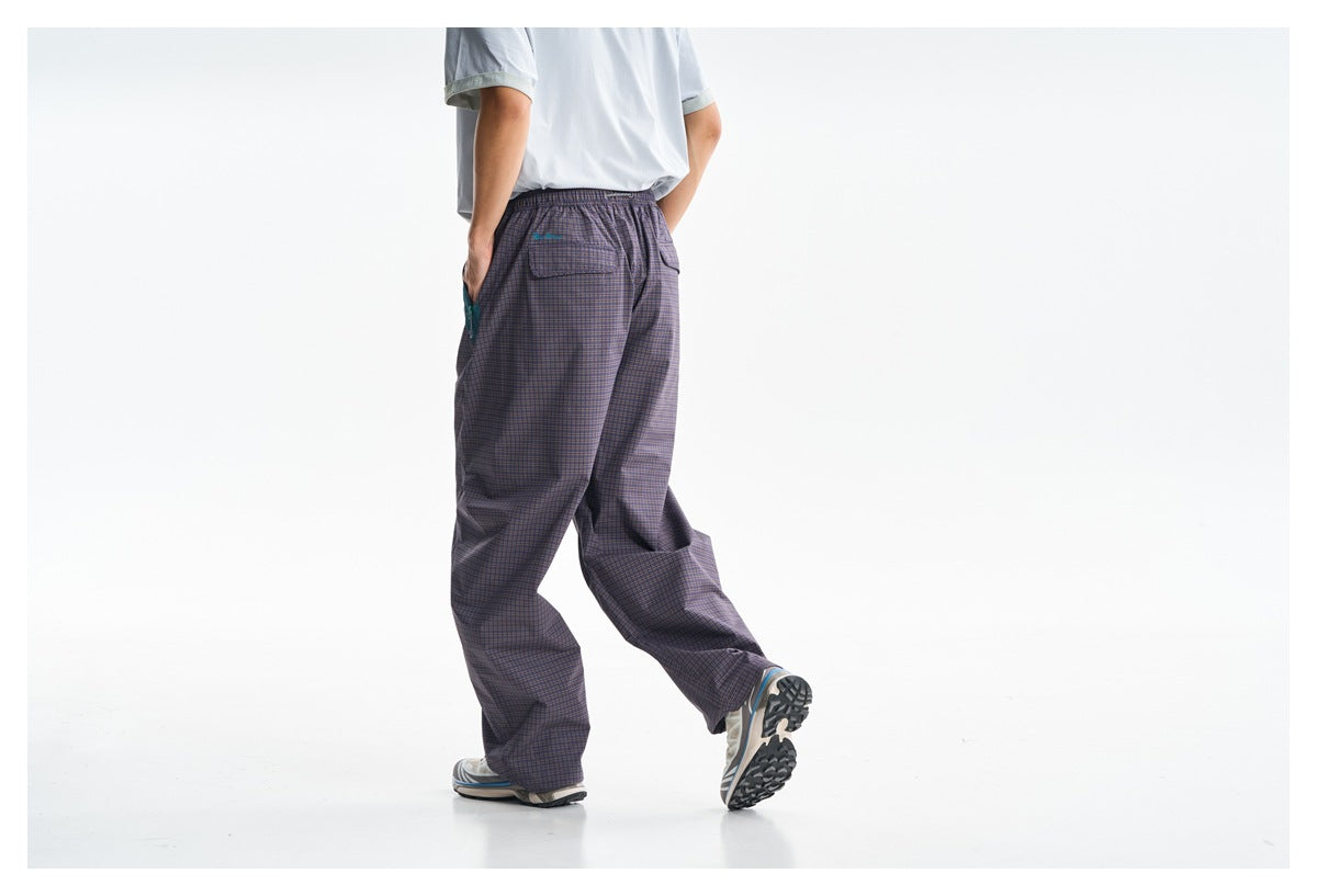 Rear view of a model wearing loose dark plaid trousers with an elastic waist and two back pockets.