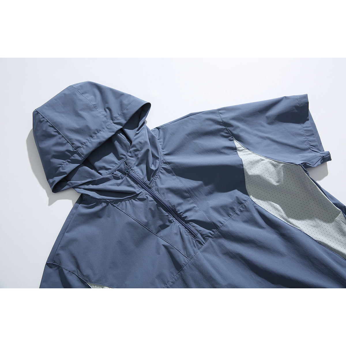 Angled flat lay of a slate-blue short-sleeve hooded pullover with a front zipper and pale perforated side panels.