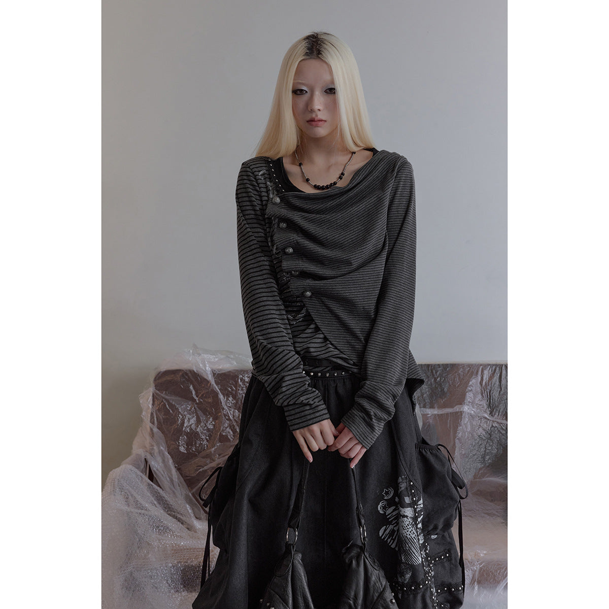 Front view of a model wearing a charcoal striped asymmetrical top with an angled button front and draped neckline.