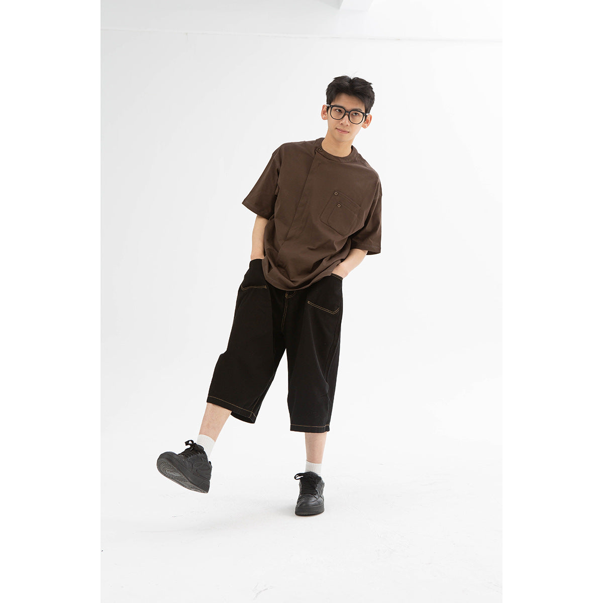 Model wearing a dark brown short-sleeve shirt with a buttoned chest pocket and black wide-leg shorts.