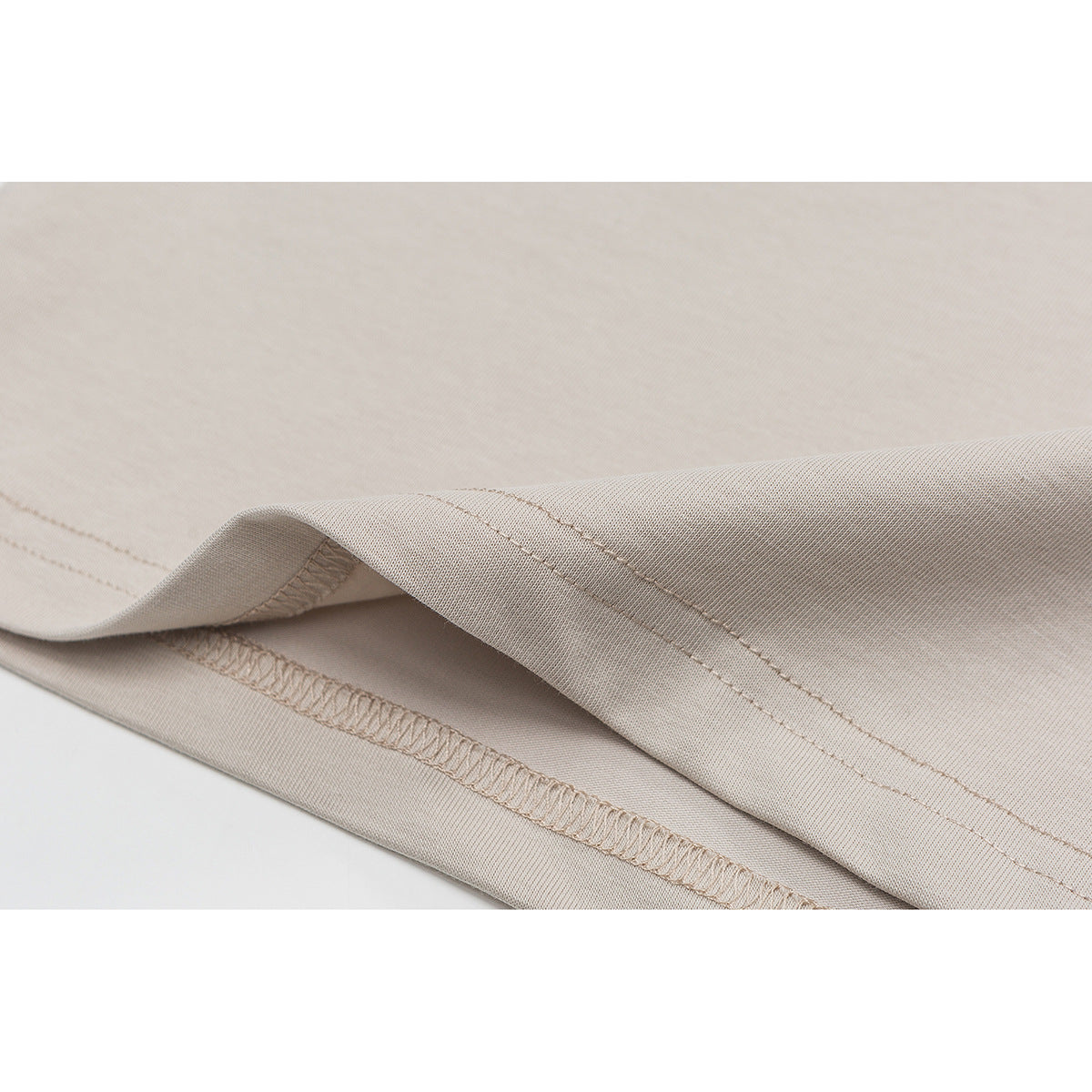 Close-up of the beige T-shirt’s double-stitched hem and overlocked seam.