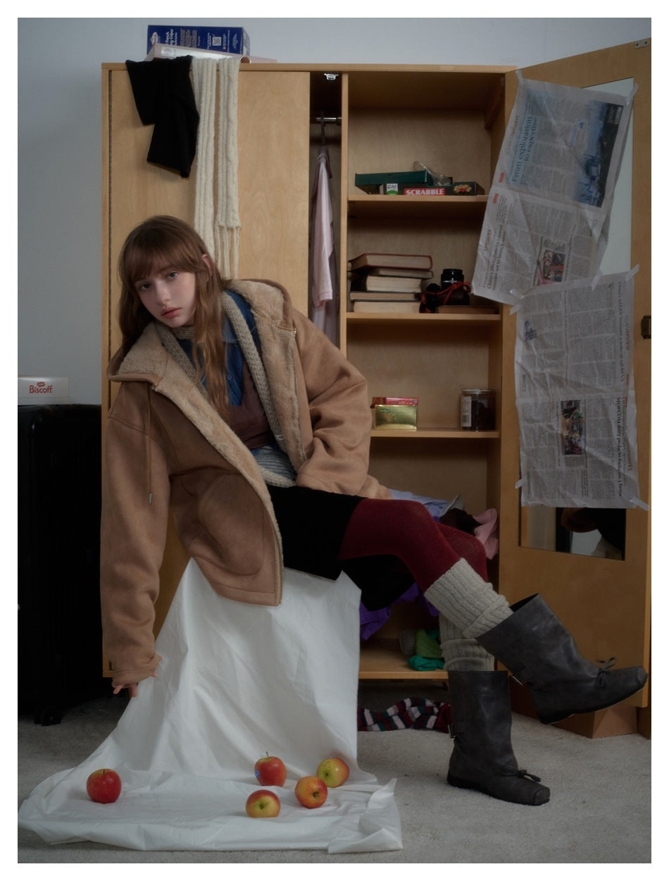 Model seated in an open tan hooded coat, showing its light lining, zipper, and large front pockets.