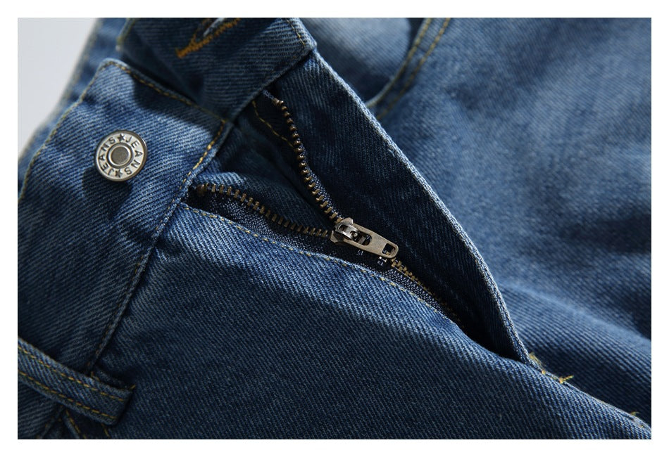 Close-up of blue denim jeans showing the waistband button, belt loop, stitching, and partly open zipper.