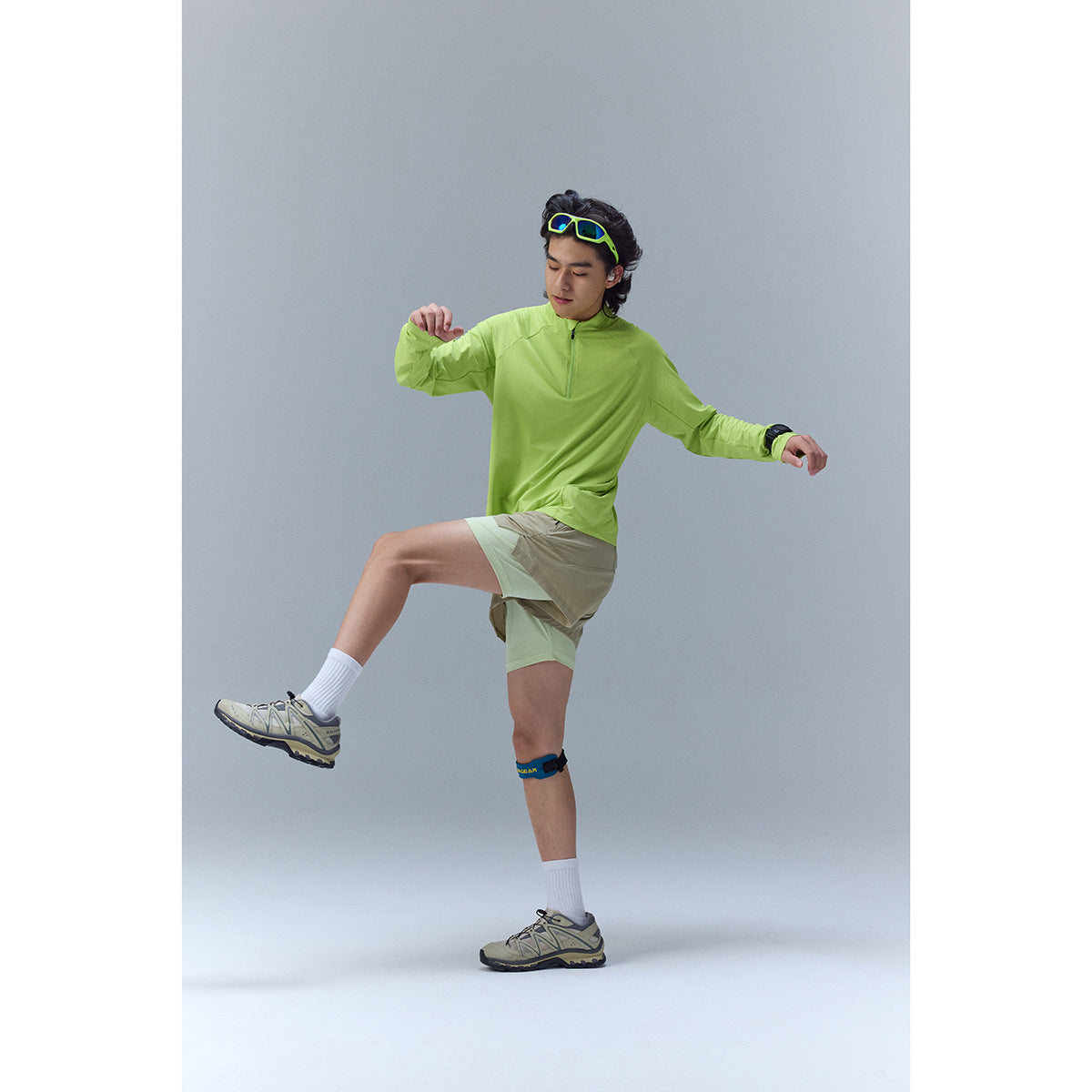 A man models a bright lime zip-neck long-sleeve top with layered beige and pale green shorts.