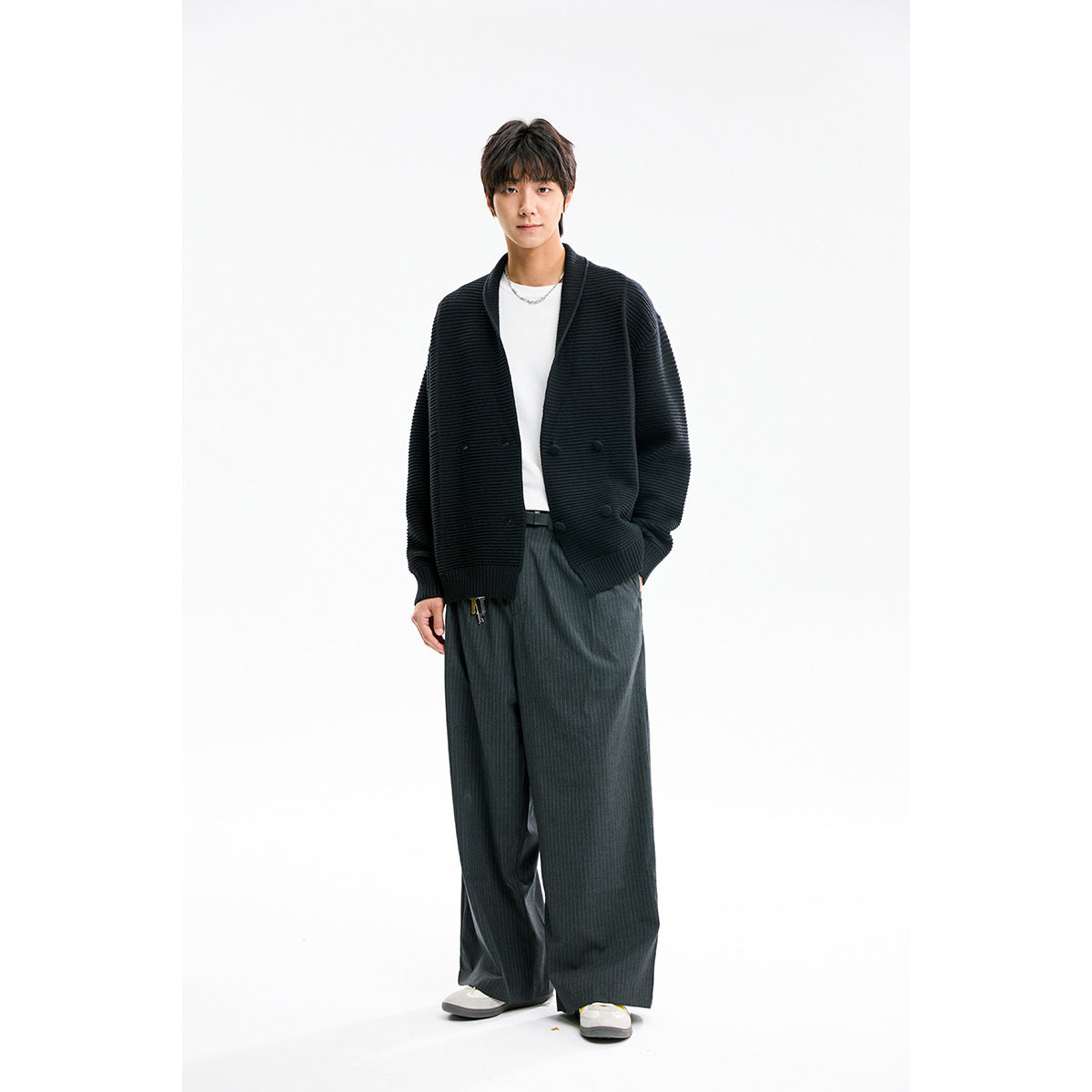 Model wearing a black ribbed shawl-collar button cardigan with a white shirt and wide gray pinstripe trousers.