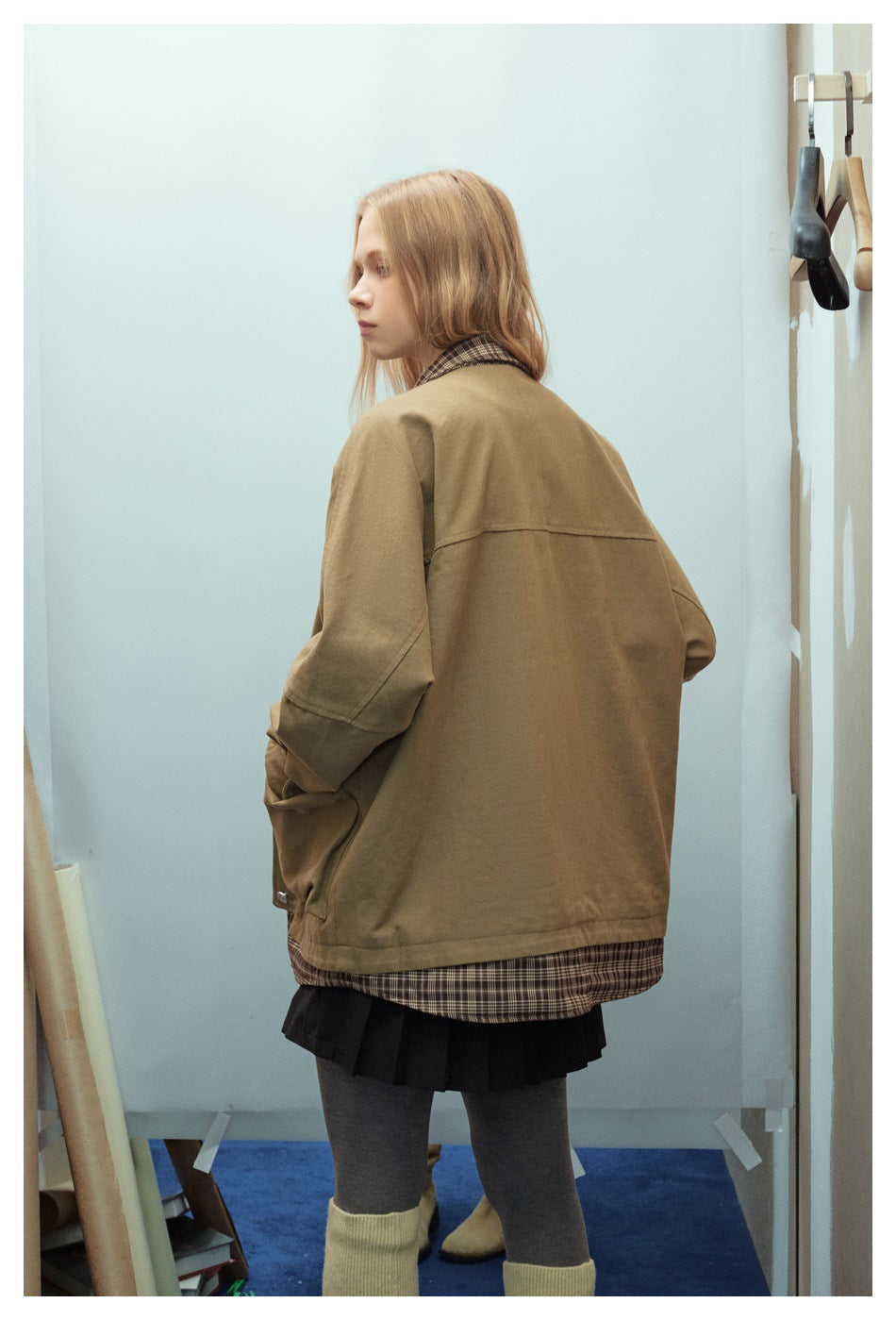 Back view of a model wearing an oversized olive-brown jacket with a plaid collar and hem.