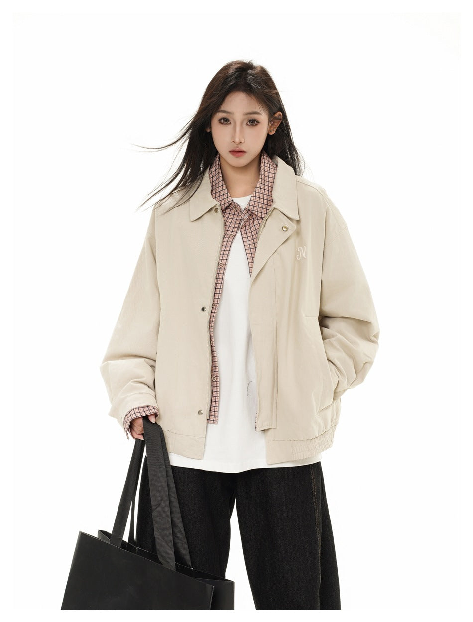 Model wearing a light beige collared jacket over a pink checked shirt and white top, with loose black jeans and a black tote.