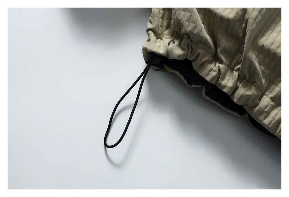 Close-up of a beige quilted jacket hem with a black drawcord loop and gathered edge.