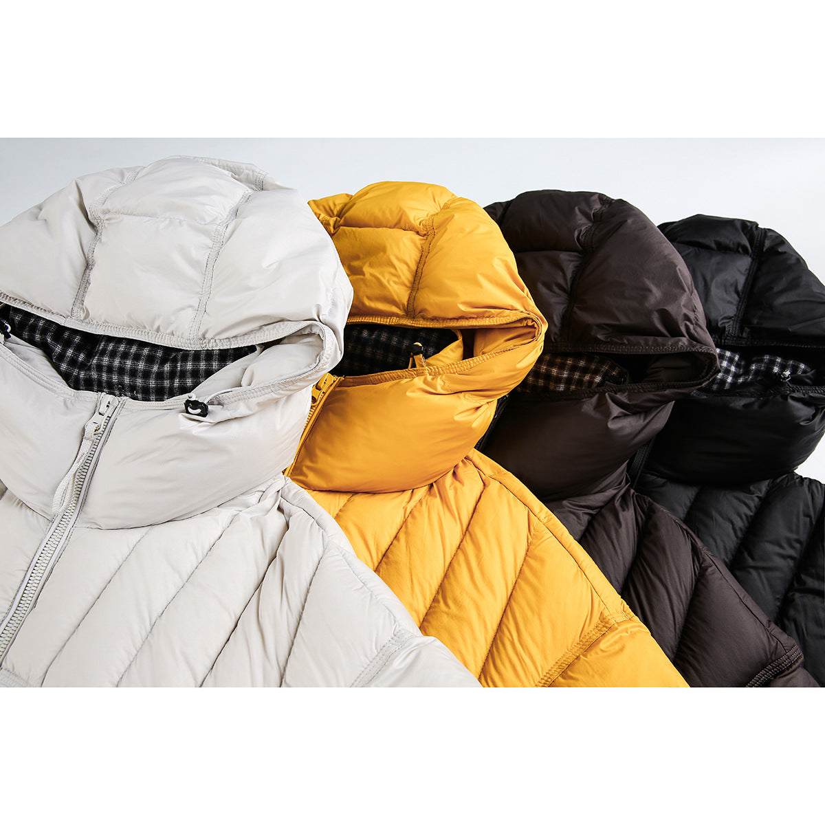 Close-up of hooded puffer jackets in white, yellow, dark brown and black, with checked lining visible.